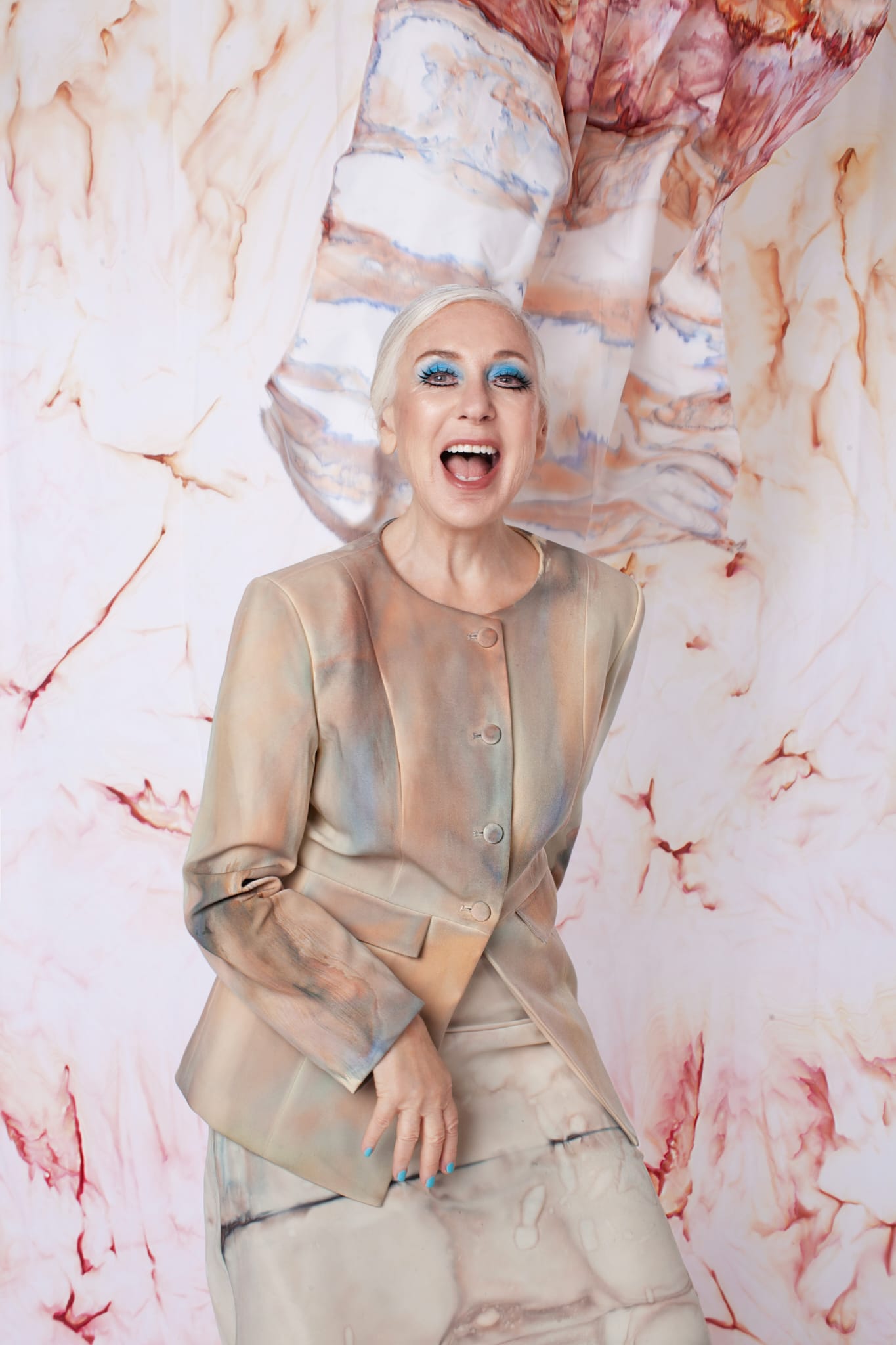 Joy Jewett, co-founder, laughing, in a painted jacket against a marbled backdrop